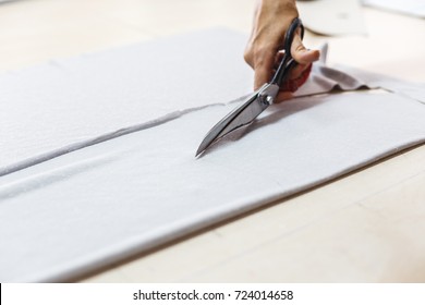Woman hands of seamstress cutting a grey fabric with scissors. Tailor working in her shop cutting a roll of grey fabric