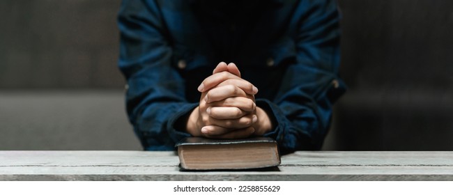 Woman hands sitting and praying with old bible in darkness on long wooden table Divine love concept, love, faith, hope - Shutterstock ID 2258855629