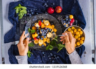 Woman hands take fruit salad from plate for breakfast. Colorful sweet healthy dessert with ripe bananas, fresh plums, delicious blueberry, yellow cherry and mint leaves. Raw vegan vegetarian food - Powered by Shutterstock