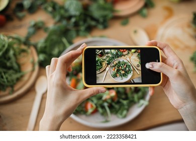 Woman hands take phone photo of food lunch or dinner. Vegetable salad, avocado, arugula tomatoes. Smartphone photography for social networks. Raw vegan vegetarian healthy food.