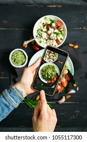 Woman Hands Takes Photography Of Food On Table With Phone. Dinner Or Lunch. Zucchini Raw Vegan Pasta With Avocado Dip Suace. Smartphone Photo For Social Networks Post. Vegetarian, Healthy, Organic 