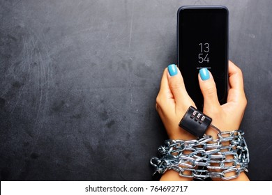 Woman hands tied with metallic chain with padlock on dark background suggesting internet or social media addiction