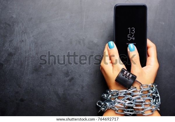 Woman hands\
tied with metallic chain with padlock on dark background suggesting\
internet or social media\
addiction