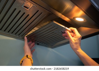 Woman hands trying to removing a filters from cooker hood for cleaning it. Clean your filters every two to three months, depending on your cooking habits. - Shutterstock ID 2182658219