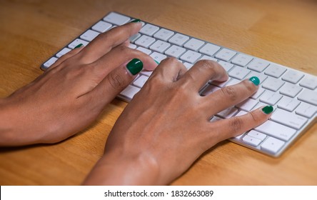 Händchen, die eine Computertastatur tippen. Weibliche Hände, die auf einer Tastatur aus Aluminium schreiben. Fingernägel sind grün gestrichen. der Schreibtisch ist aus Holz