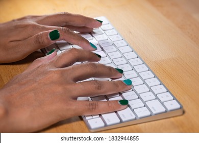 Händchen, die eine Computertastatur tippen. Weibliche Hände, die auf einer Tastatur aus Aluminium schreiben. Fingernägel sind grün gestrichen. der Schreibtisch ist aus Holz