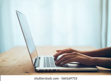 Woman hands typing on laptop keyboard at the office, Woman worker and business concept, Soft focus on vintage wooden table.