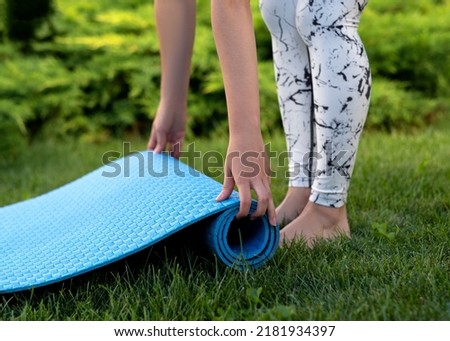 woman hands untwist a blue carpet for yoga on the green grass of leg barefoot