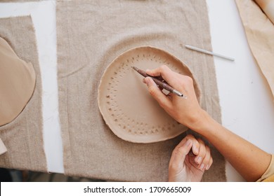 Woman hands using pen to lay down a pattern on a soft unfired clay plate. Top view. - Powered by Shutterstock