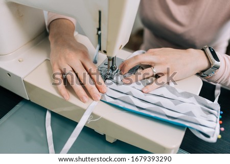Woman hands using the sewing machine to sew the face medical mask during the coronavirus pandemia. Home made diy protective mask against virus.
