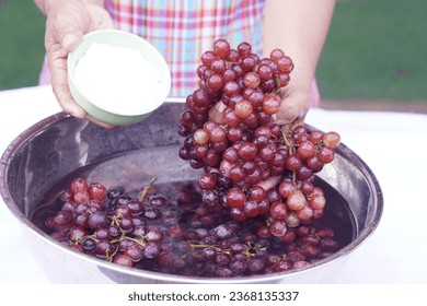 Woman hands wash grape fruits, using baking soda powder. Concept, cleaning fruits. How to wash grapes for cleanliness and safety before eating. Wash and soak in baking soda water at least 20 minutes.  - Powered by Shutterstock