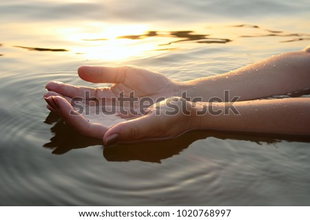 Woman hands in water inviting you over sunset golden rays.
