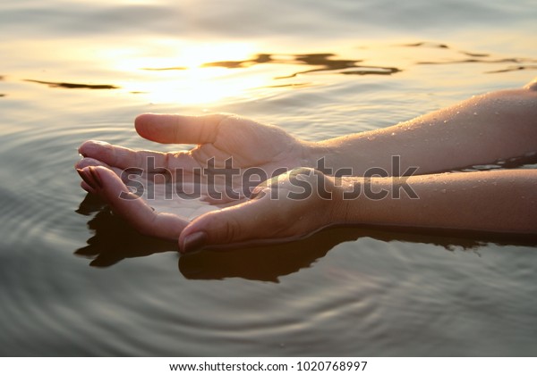 Woman hands in water inviting you over sunset\
golden rays.