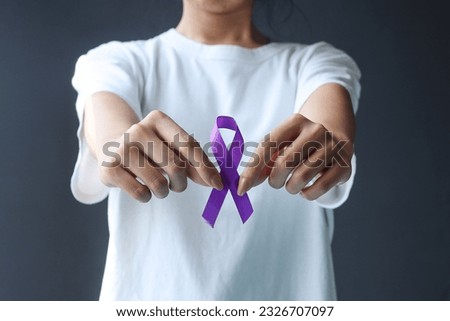 Woman hands in white t-shirt holding purple ribbon standing against dark grey background. Epilepsy awareness and World Cancer Day concept. 