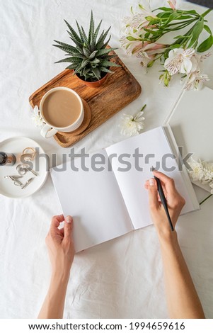 Woman hands writing in an opened book or notebook, top view flat lay. Mock up design