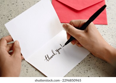 A woman hands writing a Thank You note on a greeting card with red envelope