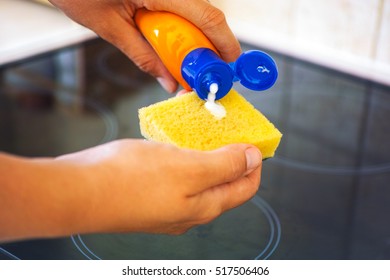 Woman hands with yellow sponge and bottle of cleaning detergent for ceramic hob.