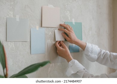 Woman Hanging Blank Paper Mock Ups On Wall. Design Paints, Reference Templates For Inspiration.Creating A Project. Architectural Or Design Bureau.