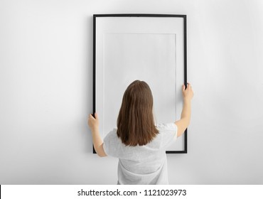 Woman Hanging Blank Photo Frame On White Wall