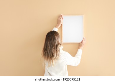 Woman Hanging Blank Photo Frame On Wall