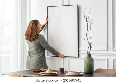 Woman hanging blank picture frame on the wall - Powered by Shutterstock