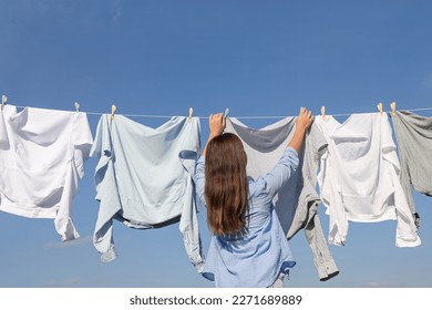 Woman hanging clothes with clothespins on washing line for drying against blue sky, back view
