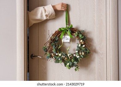 Woman hanging Easter wreath on wooden door, closeup - Shutterstock ID 2143029719