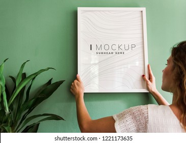 Woman Hanging A Frame Mockup On A Wall