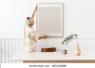 Woman hanging a photo frame on a white wall mockup