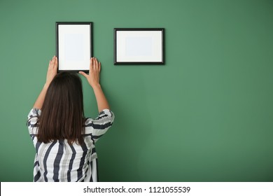 Woman Hanging Picture Frame On Color Wall