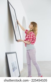 Woman Hanging Picture Frame On Wall In New House