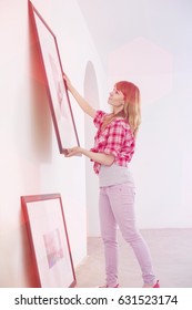 Woman Hanging Picture Frame On Wall In New House