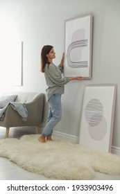 Woman hanging picture on wall in room. Interior design - Shutterstock ID 1933903496