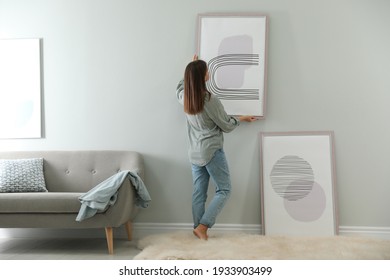 Woman hanging picture on wall in room. Interior design - Shutterstock ID 1933903499