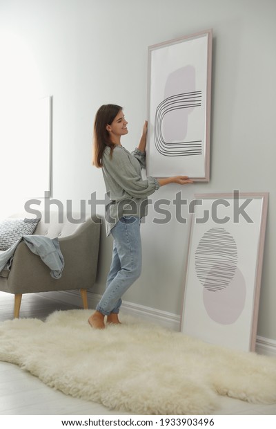 Woman\
hanging picture on wall in room. Interior\
design