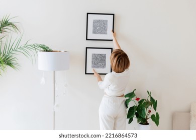 Woman hanging pictures on wall in room. Interior design - Powered by Shutterstock