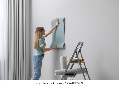 Woman hanging stylish wall paper sheet indoors - Shutterstock ID 1996882283