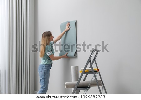 Woman hanging stylish wall paper sheet indoors