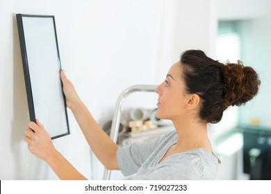 Woman Hanging Wood Frame Picture On The Wall