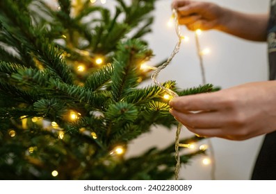 Woman hangs garland with light bulbs on a New Year tree. - Powered by Shutterstock