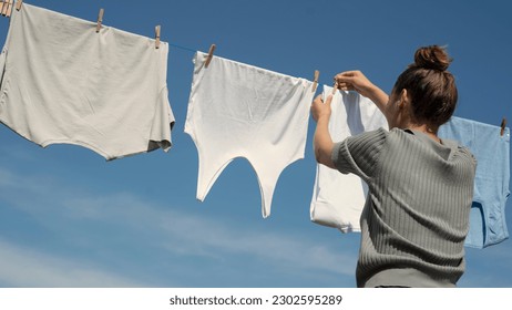 Woman hangs laundry on clothesline - Shutterstock ID 2302595289