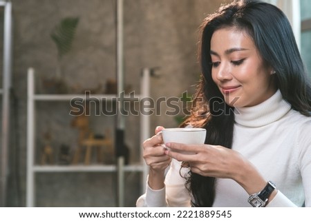 A woman happily drinking her morning coffee to warm and refresh herself at a cafe in winter, she thinks about work while drinking coffee.