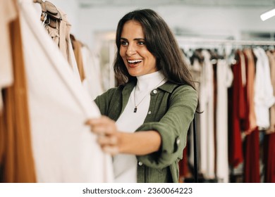 Woman happily shops for clothing in a fashionable boutique. Female customer getting excited as she sees the perfect outfit on the racks of a fashion store. - Powered by Shutterstock