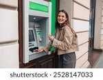 Woman happily withdrawing cash from an atm while holding her phone on a busy city street, enjoying modern electronic banking