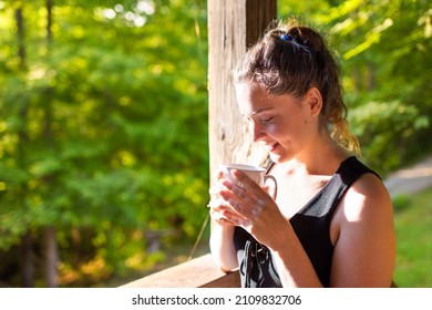 Woman happy smiling drinking coffee or tea with sunrise sunlight on rustic wooden porch of house in morning wooden cabin cottage rural countryside retreat in summer - Powered by Shutterstock