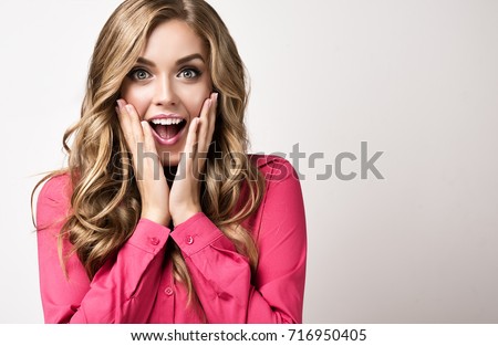 Woman  happy and surprised shouts holds cheeks by hand .Beautiful girl  with curly hair  pointing to looking right . Presenting your product. Expressive facial expressions businesswoman  .