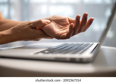 A woman has finger and hand pain after using a computer for a long time. Pain in wrist while using laptop, carpal tunnel syndrome. - Shutterstock ID 2092367314