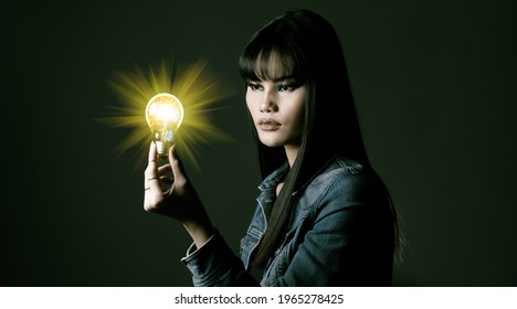 Woman Has Long Straight Black Hair Hold Light Bulb As Problem Solve And Thinking Idea. Portrait Of Asian Female Wear Many Rings Over Dark Green Tone Background, Copy Space