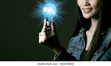 Woman Has Long Straight Black Hair Hold Light Bulb As Problem Solve And Thinking Idea. Portrait Of Asian Female Wear Many Rings Over Dark Green Tone Background, Copy Space