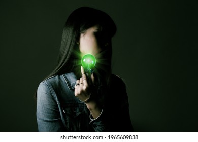 Woman Has Long Straight Black Hair Hold Light Bulb As Problem Solve And Thinking Idea. Portrait Of Asian Female Wear Many Rings Over Dark Green Tone Background, Copy Space